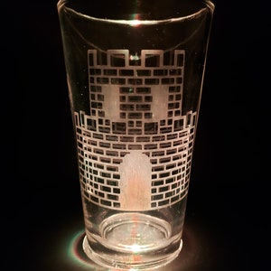 May include: A clear glass pint glass with an etched design of a castle on the front.
