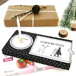 May include: A wrapped gift box with a pine cone and sprig of greenery, a black polka dot box with a card that says "Ich hab da was für dich", and a small Christmas tree on a white surface. A package of strawberry yogurt is also visible.