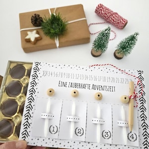 Może przedstawiać: Ręcznie robiony kalendarz adwentowy z niemieckim tekstem "Eine Zauberhafte Adventszeit". Kalendarz ma cztery ponumerowane sloty, drewniane koraliki i ołówek. Inne elementy to zapakowany prezent, miniaturowe choinki i pudełko czekoladek.