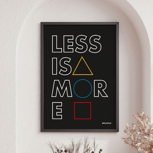 May include: A black and white poster with the text "LESS IS MORE" in white letters. The letters are outlined in black and have colored geometric shapes behind them. The poster is hanging on a white wall in a room with a rocking chair and a coffee table.