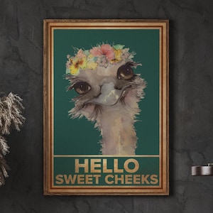 Puede incluir: Una ilustración de acuarela de una avestruz con una corona de flores en la cabeza. La avestruz está mirando al espectador con una expresión juguetona. El fondo es de color verde azulado. El texto "Hello Sweet Cheeks" está escrito en letras doradas debajo de la avestruz.
