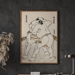 May include: A black and white illustration of two sumo wrestlers in a fighting pose. The image is framed in a wooden frame and has Japanese text in the top corners.