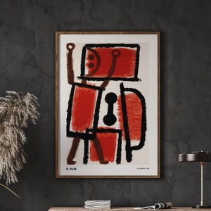 Puede incluir: Una impresión de arte abstracto enmarcada que presenta un diseño geométrico rojo y negro. La impresión se titula "Ad Parnassum" de Paul Klee y está fechada en 1932.