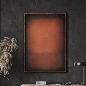 May include: A framed abstract painting with a dark brown background and a horizontal band of orange in the middle. The painting is hanging on a dark grey wall above a wooden shelf with a lamp and books.