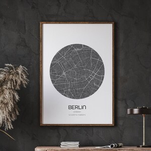 Op de afbeelding: Een zwart-witte printbare kaart van Berlijn, Duitsland, met de naam van de stad en de coördinaten onder de kaart. De kaart is ingelijst en hangt aan een donkergrijze muur.
