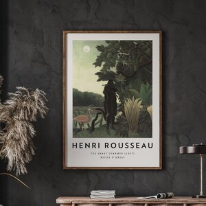 Op de afbeelding: Een poster met een schilderij van Henri Rousseau met de titel "De slangenvanger" (1907). Het schilderij toont een donkerhuidige figuur in een jungle-omgeving, omringd door weelderig groen en een roze vogel.
