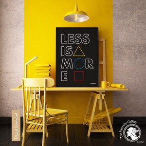 May include: A black and white printable wall art print with the text "Less is More" in a geometric design with a yellow triangle, blue circle, and red square. The print is displayed on a yellow wall in a home office setting.