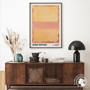 May include: A minimalist abstract painting by Mark Rothko, featuring three horizontal bands of color: a pale yellow, a pink, and a darker yellow. The painting is framed in black and displayed on a wall above a wooden cabinet.