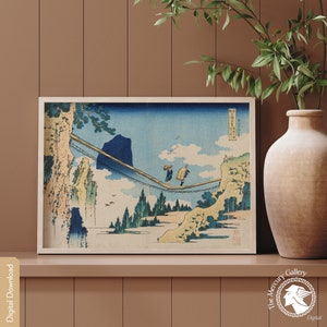 Könnte beinhalten: Ein gerahmter Druck eines japanischen Holzschnitts, der eine Berglandschaft mit einer Brücke und zwei Personen zeigt, die darüber gehen. Der Druck ist in Blautönen, Grün- und Brauntönen gehalten.