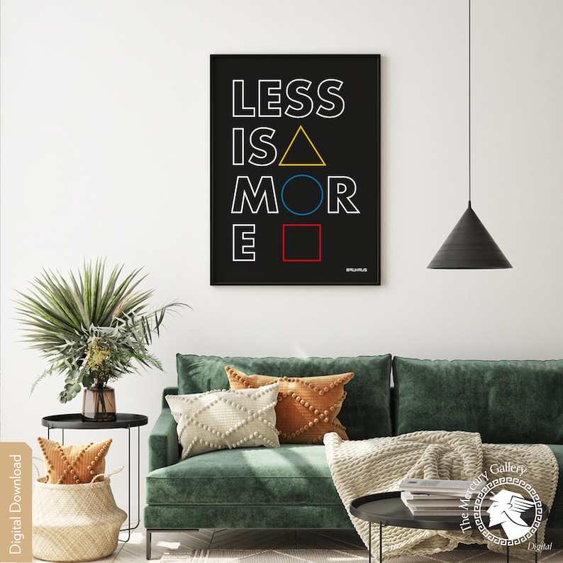 May include: A black and white poster with the text "LESS IS MORE" in white with a yellow triangle, blue circle, and red square. The poster is framed and hanging on a white wall above a green sofa with pillows.