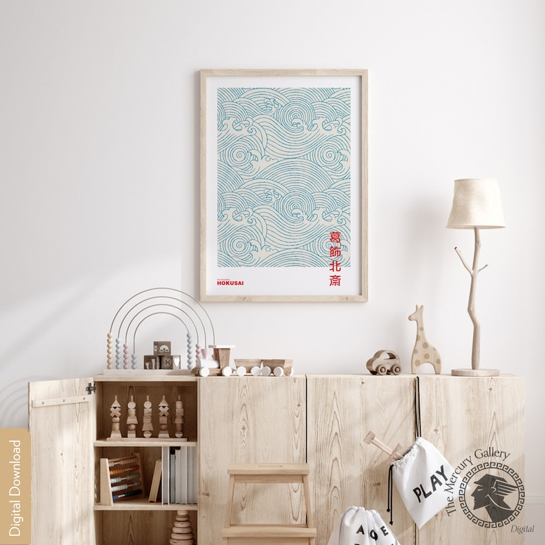 May include: A framed print of a blue and white wave pattern with Japanese text in red. The print is titled "Hokusai" and is hanging on a white wall in a room with a wooden cabinet and a lamp.
