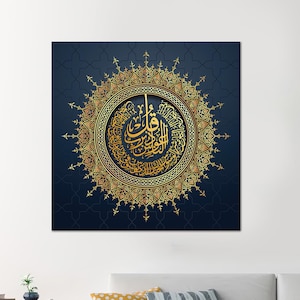 May include: A square wall art piece with gold calligraphy in a circular design, set against a dark blue background with a repeating pattern. The artwork is displayed above a white sofa with decorative cushions.