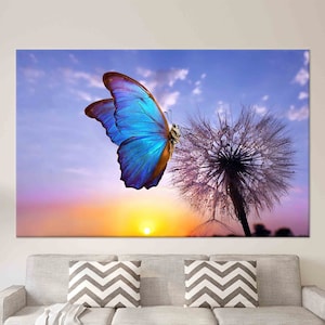 May include: A blue butterfly with brown wings perched on a white dandelion with dew drops. The background is a colourful sunset with clouds.