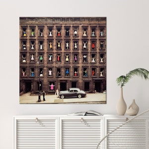 May include: A vintage photograph of a city building with multiple windows. Each window has a person in a colourful dress looking out. A black car is parked in front of the building.