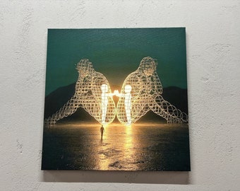 Puede incluir: Una escultura de alambre de metal brillante que representa dos figuras que se miran, con una figura más pequeña caminando hacia ellas en primer plano. La escultura está situada sobre un fondo verde oscuro con un paisaje desértico.