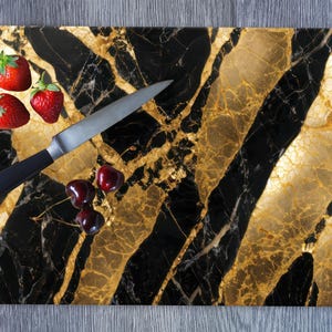 May include: A black and gold marble cutting board with a knife and red strawberries and cherries on top.
