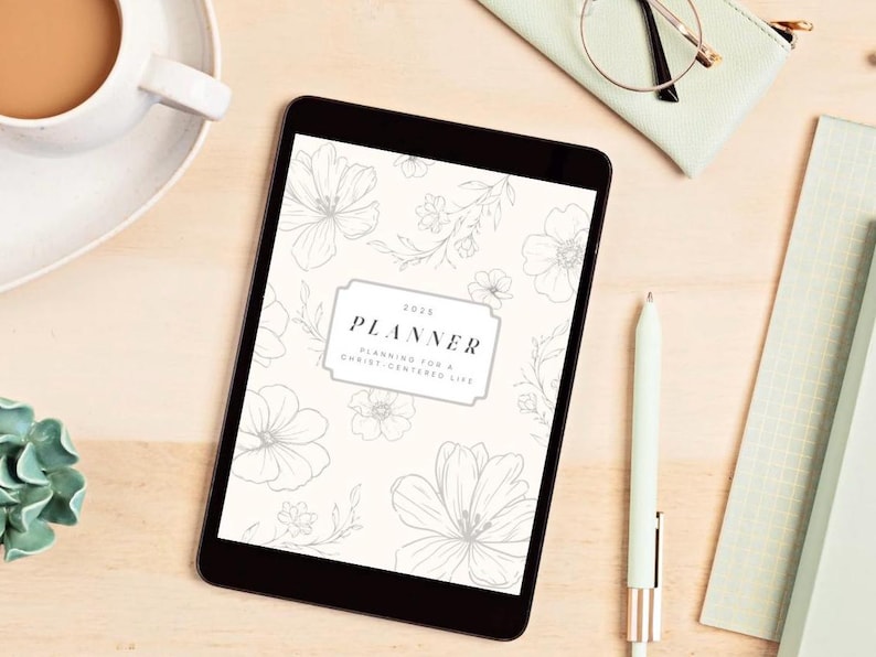 K&ouml;nnte beinhalten: Ein Tablet-Computer zeigt einen 2025-Planer mit floralen Illustrationen. Der Einband des Planers tr&auml;gt den Text "PLANNER" und "Planning for a Christ-centered life". Ein Stift, eine Brille und eine Tasse Kaffee sind ebenfalls auf der Holzoberfl&auml;che zu sehen.