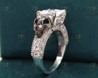 May include: A silver ring with a large, clear, pear-shaped gemstone and a black skull design. The ring is set with smaller, clear gemstones around the band.