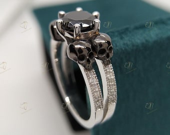 May include: A black diamond engagement ring with two skull-shaped bands. The ring is set in white gold and features a pave setting of smaller diamonds on the bands.