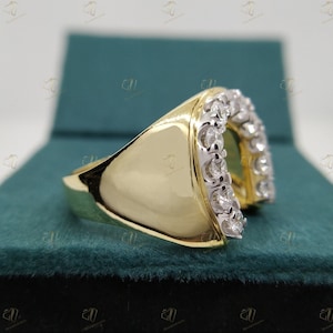 May include: A gold ring with a horseshoe design set with small diamonds. The ring is on a green velvet background.