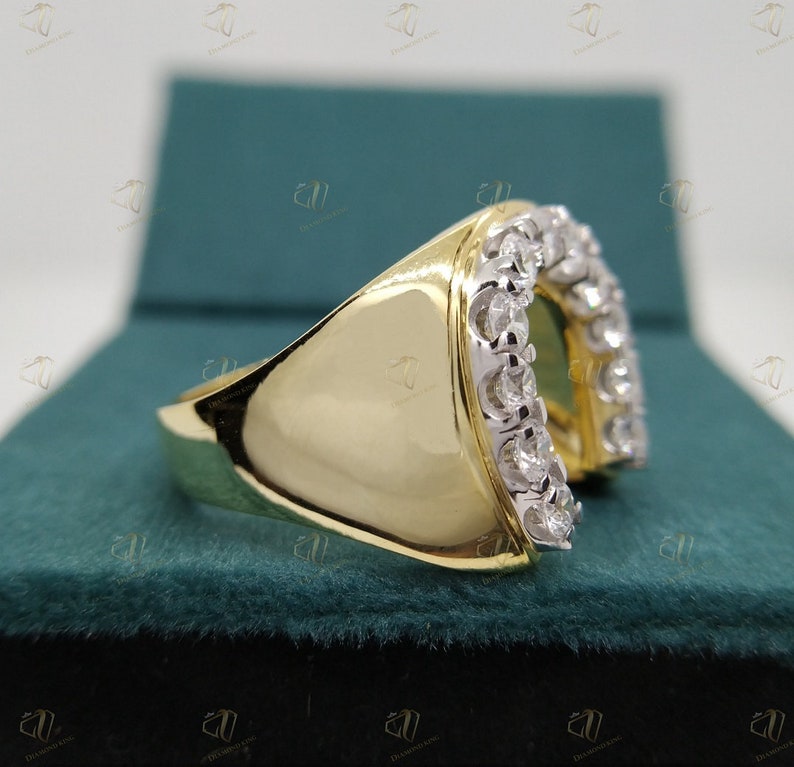 May include: A gold ring with a horseshoe design set with small diamonds. The ring is on a green velvet background.