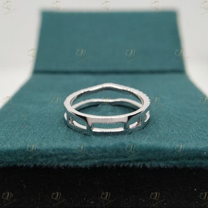 May include: A silver ring with a geometric design. The ring is set on a green velvet background.