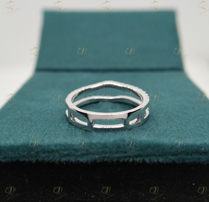 May include: A silver ring with a geometric design. The ring is set on a green velvet background.