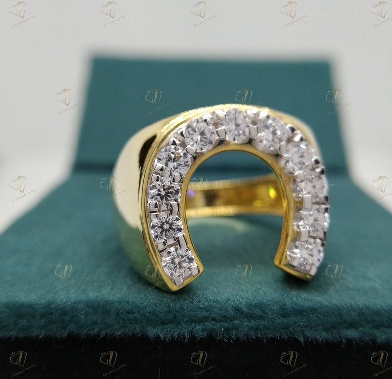May include: A gold ring with a horseshoe design set with clear round stones. The ring is displayed in a green velvet box.