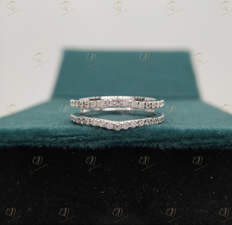 May include: A delicate, curved, diamond ring enhancer with a row of small diamonds on each side. The enhancer is in a ring box with a green velvet lining.