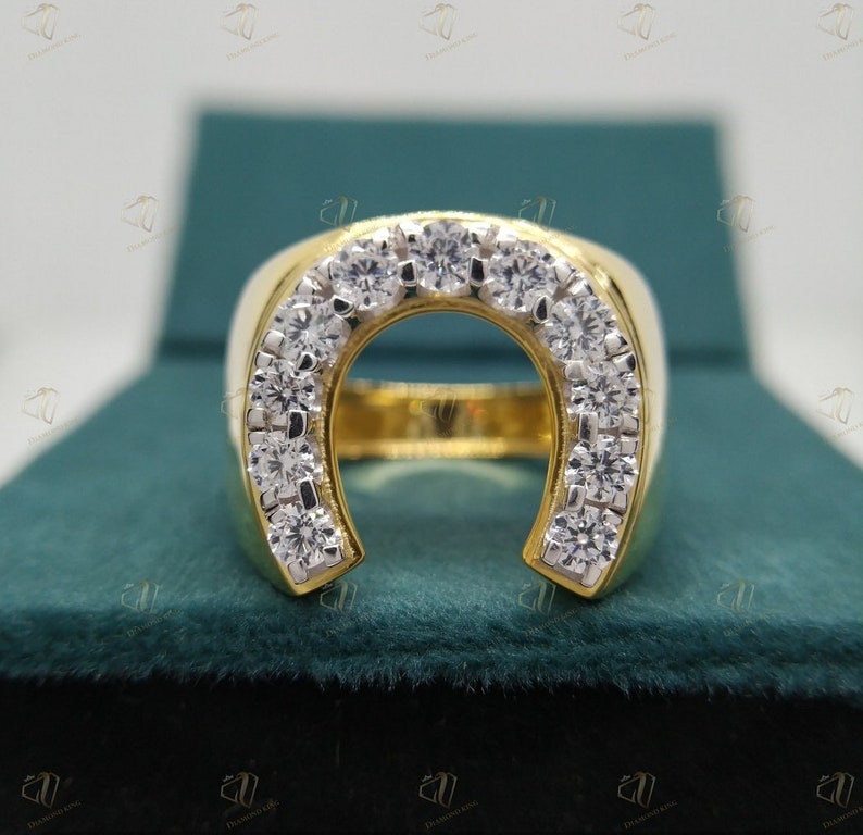 May include: A gold horseshoe ring with a row of clear diamonds around the horseshoe. The ring is sitting in a green velvet box.