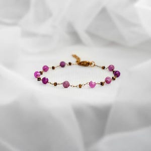 Peut inclure: Un bracelet délicat de couleur or, orné de perles roses et marron alternées. Le bracelet est orné de plusieurs pierres précieuses roses vibrantes, créant un accessoire subtil mais élégant. Le fermoir est de couleur or.