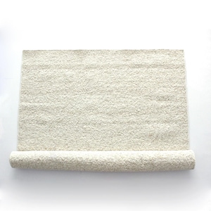 Könnte beinhalten: Ein rechteckiger, cremefarbener Teppich mit strukturierter Oberfläche. Der Teppich ist unten teilweise aufgerollt, wodurch seine Dicke sichtbar wird. Die neutrale Farbe und das schlichte Design machen ihn für verschiedene Einrichtungsstile geeignet.