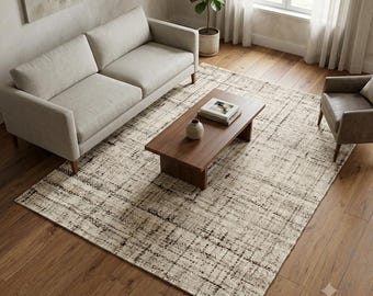 May include: A rectangular area rug featuring a textured, cross-hatched pattern in shades of cream, beige, and dark brown. The rug is positioned on a wooden floor beneath a light-colored sofa, a wooden coffee table, and a single armchair in a room.