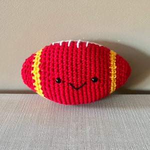 May include: A red and yellow crocheted football with a white stitched seam and a smiling face.
