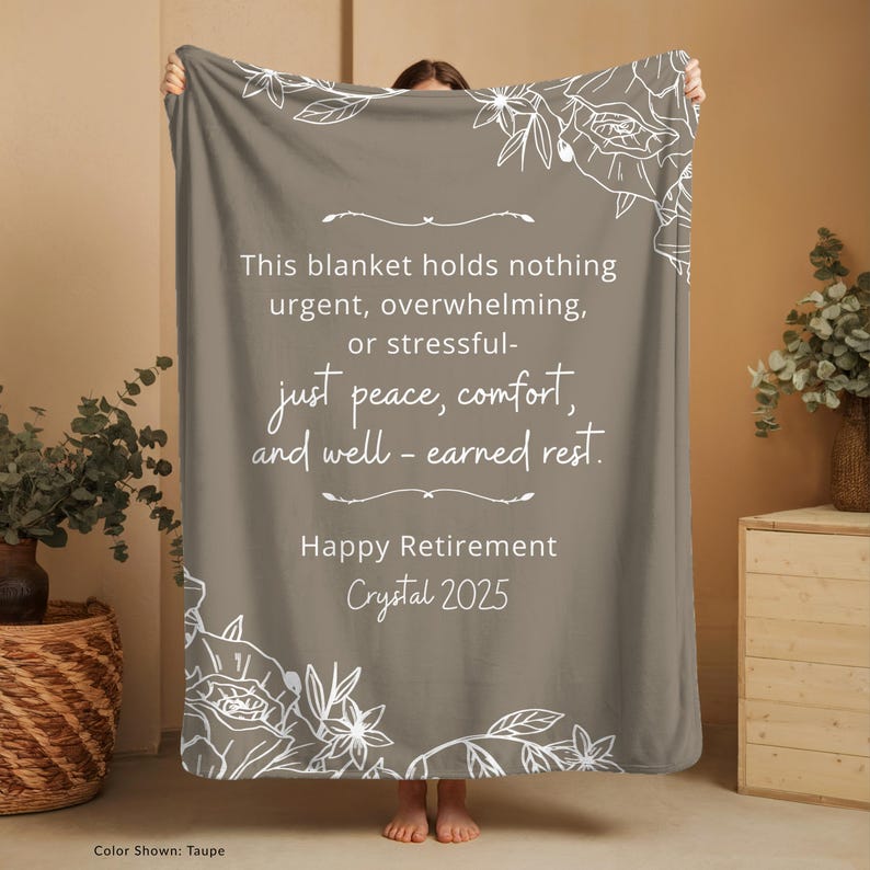 Peut inclure: Couverture taupe avec des motifs floraux blancs et du texte. Le texte se lit comme suit : &laquo; Ce plaid ne contient rien d'urgent, de bouleversant ou de stressant - juste la paix, le confort et le repos bien m&eacute;rit&eacute;. Joyeux d&eacute;part &agrave; la retraite Crystal 2025."