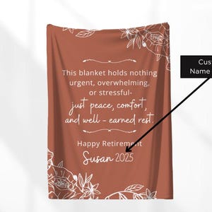 Peut inclure: Une couverture de couleur rouille avec des motifs floraux blancs et du texte. Le texte dit : &laquo; Ce plaid ne contient rien d'urgent, de bouleversant ou de stressant - juste la paix, le confort et le repos bien m&eacute;rit&eacute;. &raquo; Il dit aussi &laquo; Happy Retirement Susan 2025 &raquo;.