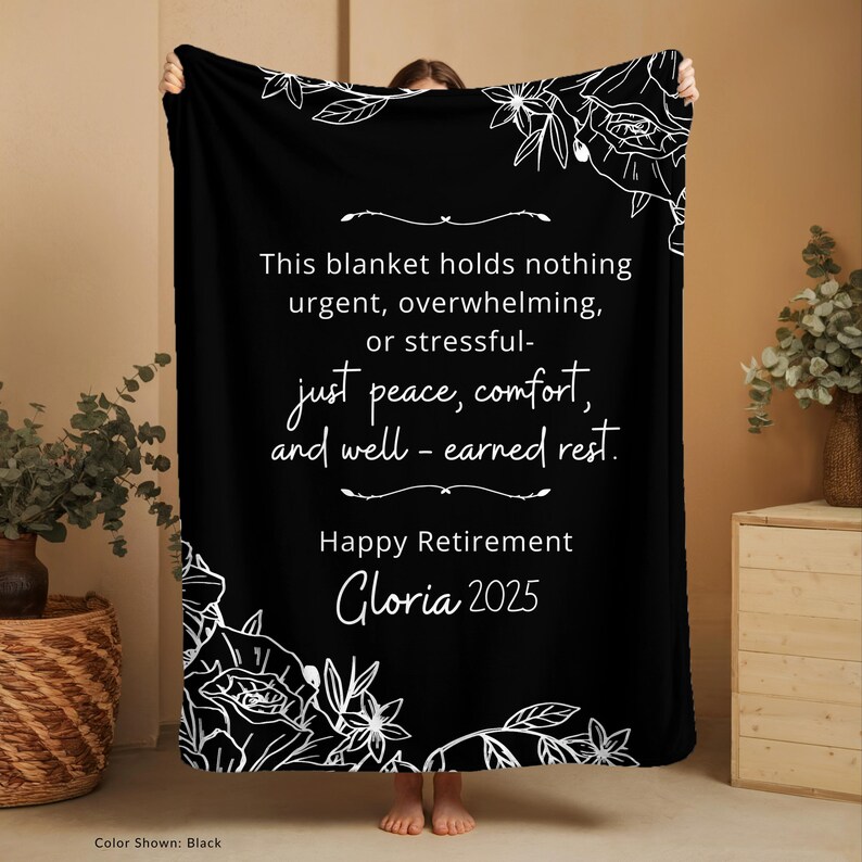 Peut inclure: Couverture noire avec des motifs floraux blancs dans les coins et du texte. Le texte se lit comme suit : "Ce plaid ne contient rien d'urgent, de bouleversant ou de stressant - juste la paix, le confort et le repos bien m&eacute;rit&eacute;. Joyeux d&eacute;part &agrave; la retraite Gloria 2025."