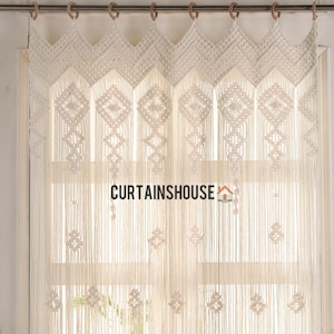 以下が含まれることがあります： 幾何学模様の白いマクラメカーテン。カーテンは木製のリングが付いた金属製の棒にかけられています。カーテンはコットンコードで作られており、フリンジのついた裾があります。