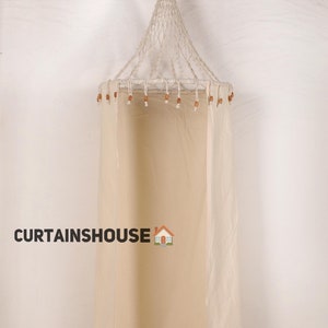 May include: A white canvas changing room with a white rope and wooden bead canopy. The changing room is freestanding and has a simple design.