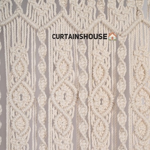 K&ouml;nnte beinhalten: Nahaufnahme einer Makramee-Wandbeh&auml;nge aus nat&uuml;rlichem Baumwollseil. Die Beh&auml;nge weist ein sich wiederholendes Muster aus Diamanten und Kreisen auf. Der Text "CURTAINS HOUSE" ist im Bild sichtbar.