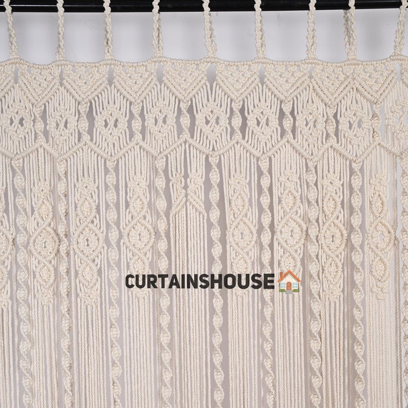 K&ouml;nnte beinhalten: Ein wei&szlig;er Makramee-Vorhang mit geometrischem Muster. Der Vorhang ist aus Baumwollschnur gefertigt und hat einen Fransen unten. Der Text "CURTAINS HOUSE" ist unten in der Mitte des Bildes sichtbar.