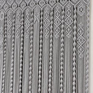 May include: A grey macrame wall hanging featuring a wooden rod at the top with loops. The design includes intricate knotted patterns, diamond-shaped geometric motifs, and long vertical strands of cord with repeating knot details throughout the piece.
