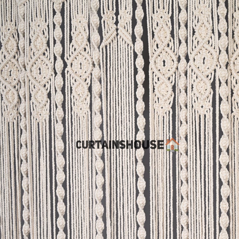 K&ouml;nnte beinhalten: Ein wei&szlig;er Makramee-Vorhang mit verschiedenen Knotenmustern. Der Vorhang ist aus Baumwollschnur gefertigt und hat einen nat&uuml;rlichen, bohemian Stil.