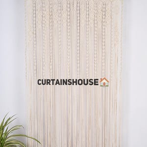 K&ouml;nnte beinhalten: Ein wei&szlig;er Makramee-Vorhang mit geometrischem Muster. Der Vorhang h&auml;ngt an einer schwarzen Stange und ist aus Baumwollschnur gefertigt. Der Text "CURTAINS HOUSE" ist unten in der Mitte des Bildes sichtbar.