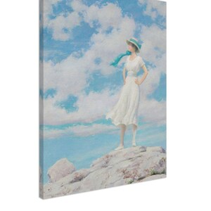 May include: A woman in a white dress and a blue scarf stands on a rocky outcrop, looking out at a blue sky with white clouds.