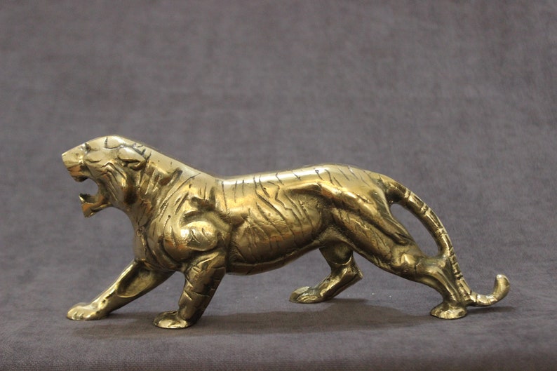 May include: A brass figurine of a tiger in a walking pose. The tiger is depicted with a detailed, textured surface and a snarling expression.
