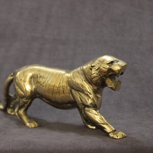 May include: A gold metal tiger figurine with a detailed, textured surface. The tiger is standing on all fours with its mouth open in a roar.