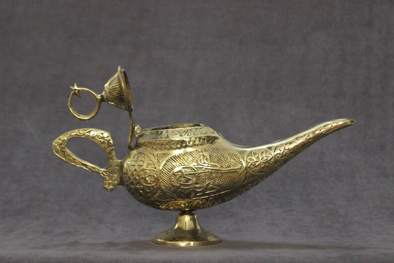 May include: A gold genie lamp with intricate floral and geometric designs. The lamp has a hinged lid and a star-shaped handle.