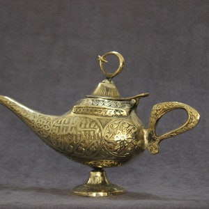 May include: A gold genie lamp with intricate engraved designs. The lamp has a spout, a handle, and a lid with a crescent moon finial.