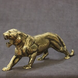 May include: A gold-colored metal figurine of a tiger in a snarling pose. The tiger is depicted with detailed features and a realistic appearance.